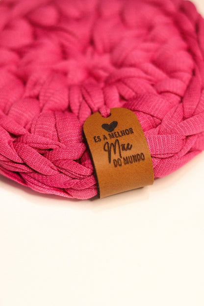 Detalhe em grande plano da etiqueta de couro em base de malha rosa com a frase És a Melhor Mãe do Mundo.