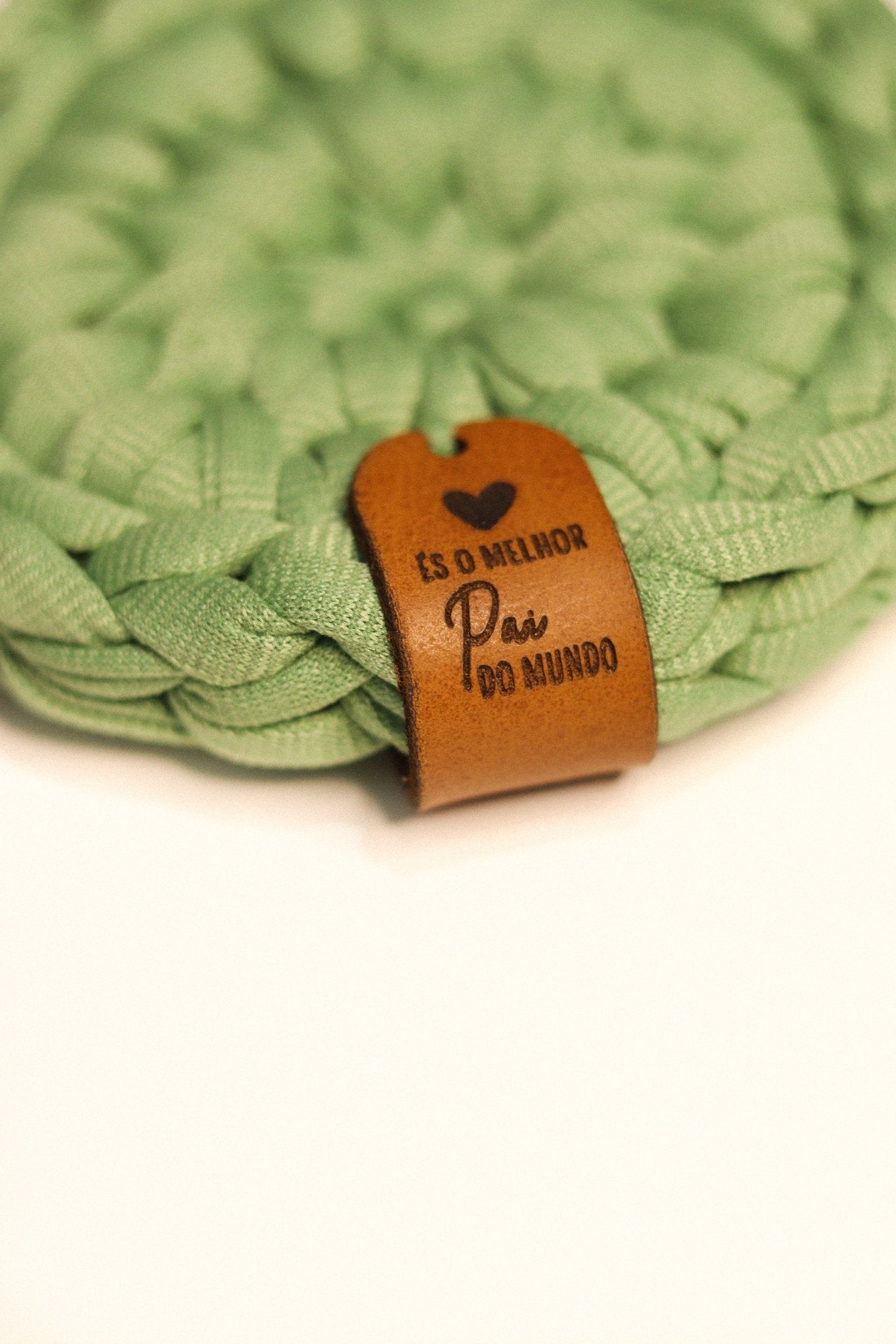 Detalhe da etiqueta de couro personalizada com a frase És o Melhor Pai do Mundo em base de malha verde.