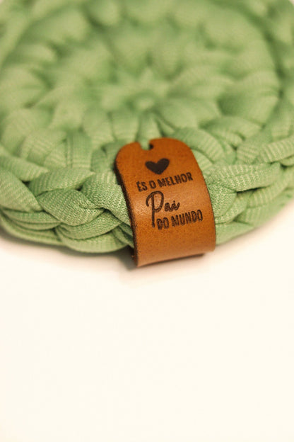 Detalhe da etiqueta de couro personalizada com a frase És o Melhor Pai do Mundo em base de malha verde.