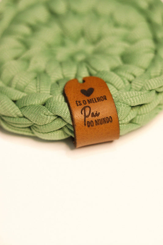 Detalhe da etiqueta de couro personalizada com a frase És o Melhor Pai do Mundo em base de malha verde.