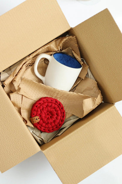 Conjunto de presente com caneca branca e base em malha vermelha artesanal em caixa de envio.