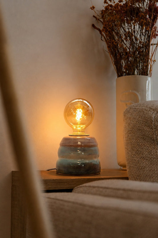 Ambientes de interior com candeeiro Aurora em mesa de apoio junto a elementos decorativos naturais.