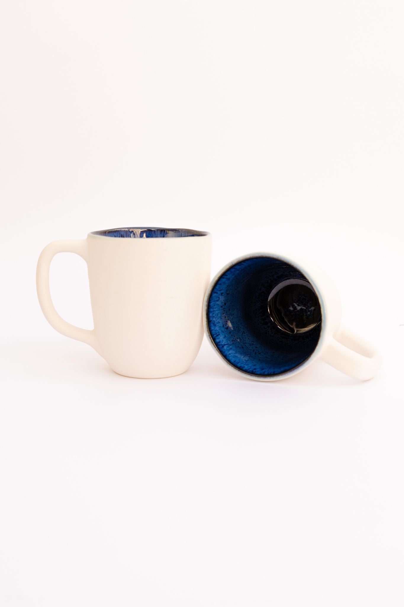 Conjunto de duas canecas CORAL em cerâmica azul e creme, evidenciando o contraste artístico entre o exterior claro e o interior esmaltado reativo.