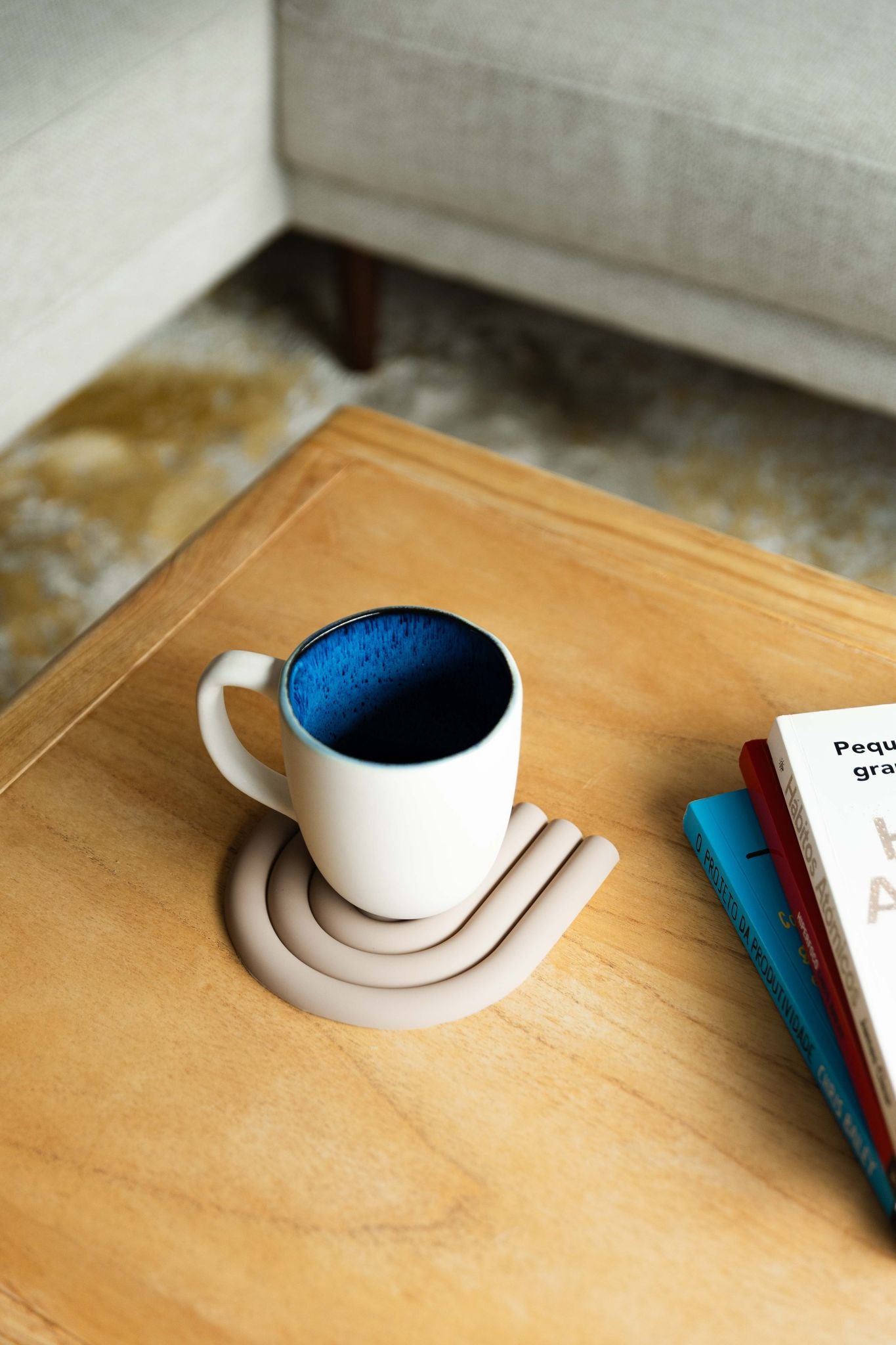 Caneca CORAL azul pousada numa mesa de centro de madeira junto a livros, criando um ambiente relaxante de leitura e conforto em casa.