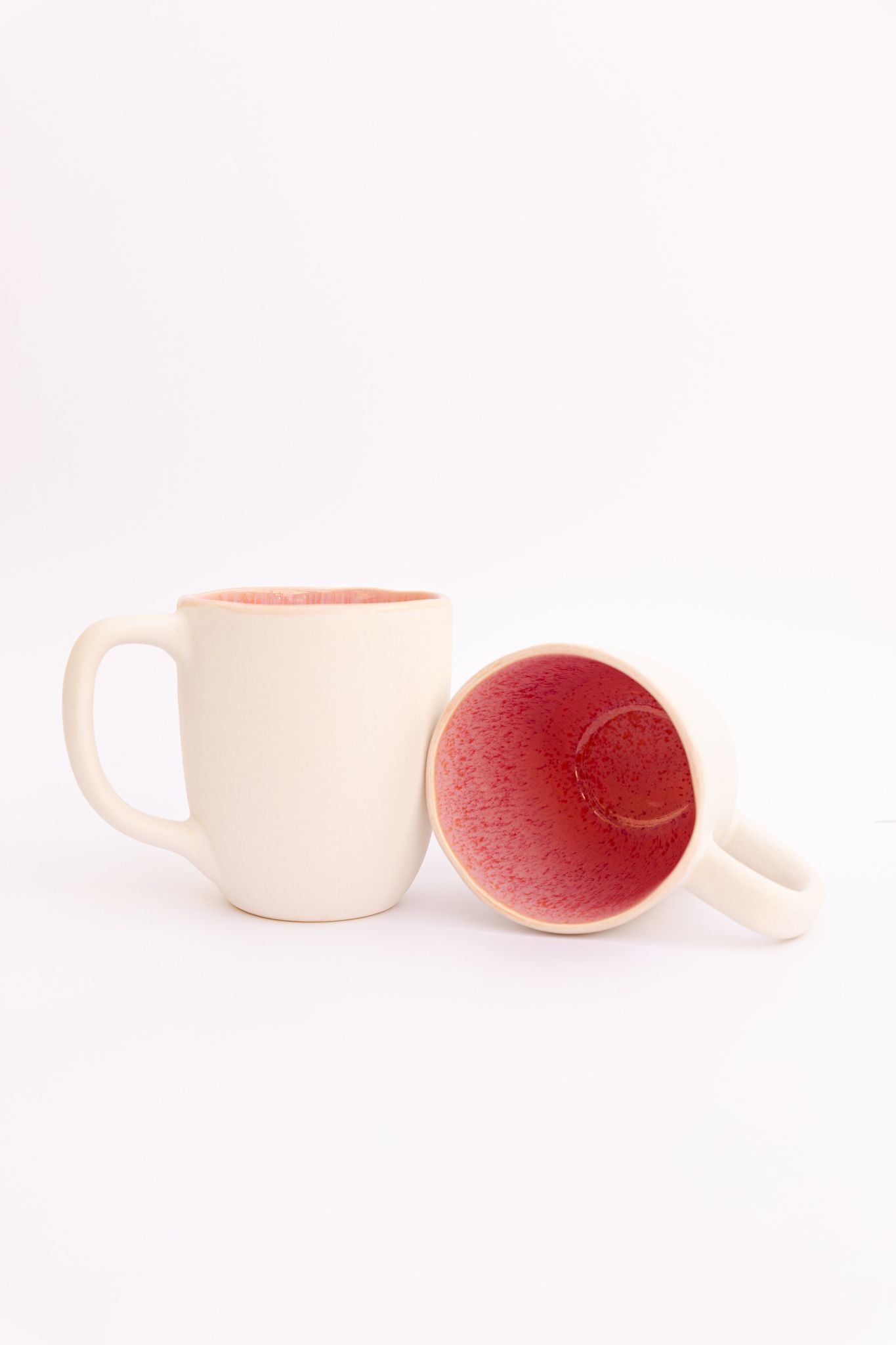 Caneca CORAL de 500ml em cerâmica, com exterior em tom branco sideral e interior rosa reativo, conjugada com uma segunda unidade deitada.