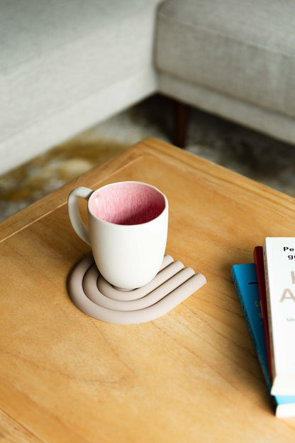 Caneca CORAL rosa integrada num cenário de sala de estar, pousada sobre uma base de design numa mesa de madeira clara.