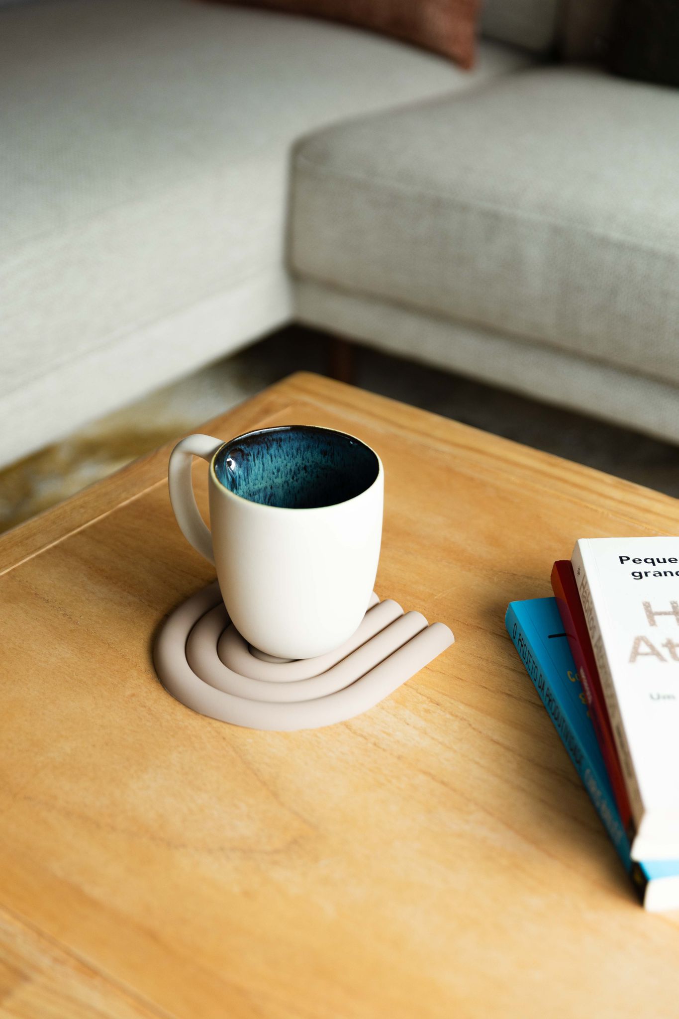 Caneca CORAL verde de 500ml pousada sobre base de silicone numa mesa de madeira, integrada num ambiente de sala de estar moderno e acolhedor.
