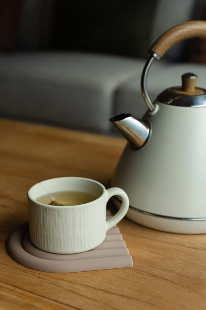 Caneca PLENO com saqueta de chá pousada sobre uma base de silicone numa mesa de madeira, num ambiente de sala de estar acolhedor e relaxante.