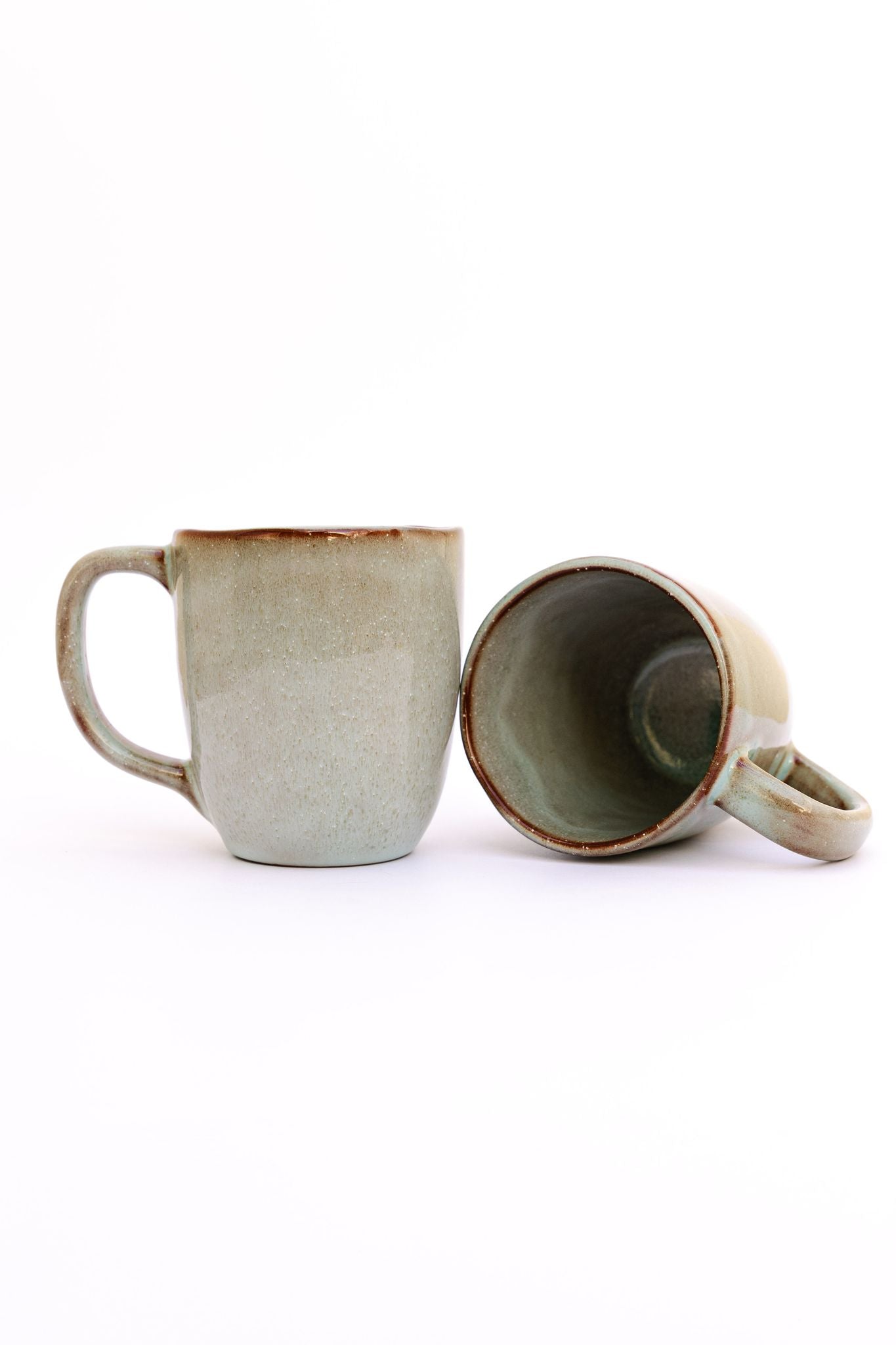 Caneca SERENO em cerâmica artesanal verde com vidrado reativo, apresentada individualmente e com uma segunda unidade para mostrar o interior e o design orgânico.