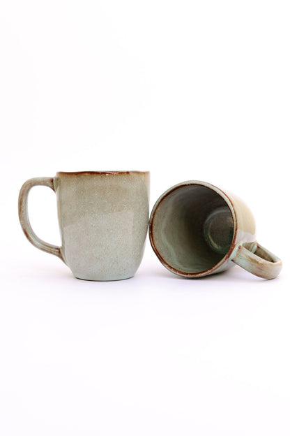 Caneca SERENO em cerâmica artesanal verde com vidrado reativo, apresentada individualmente e com uma segunda unidade para mostrar o interior e o design orgânico.