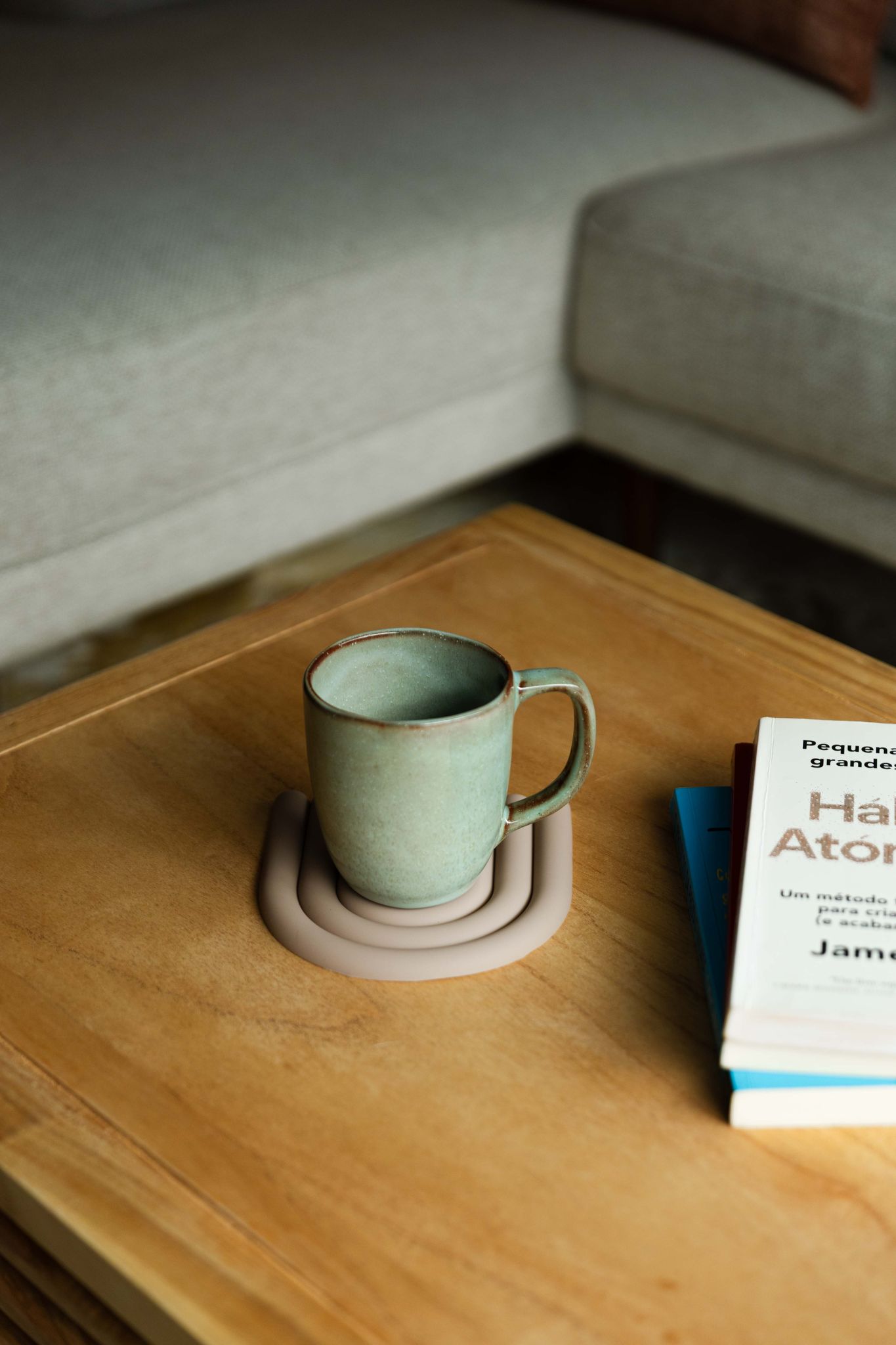 Caneca SERENO verde pousada sobre uma base de design numa mesa de madeira junto a livros, evocando um momento de leitura e tranquilidade.