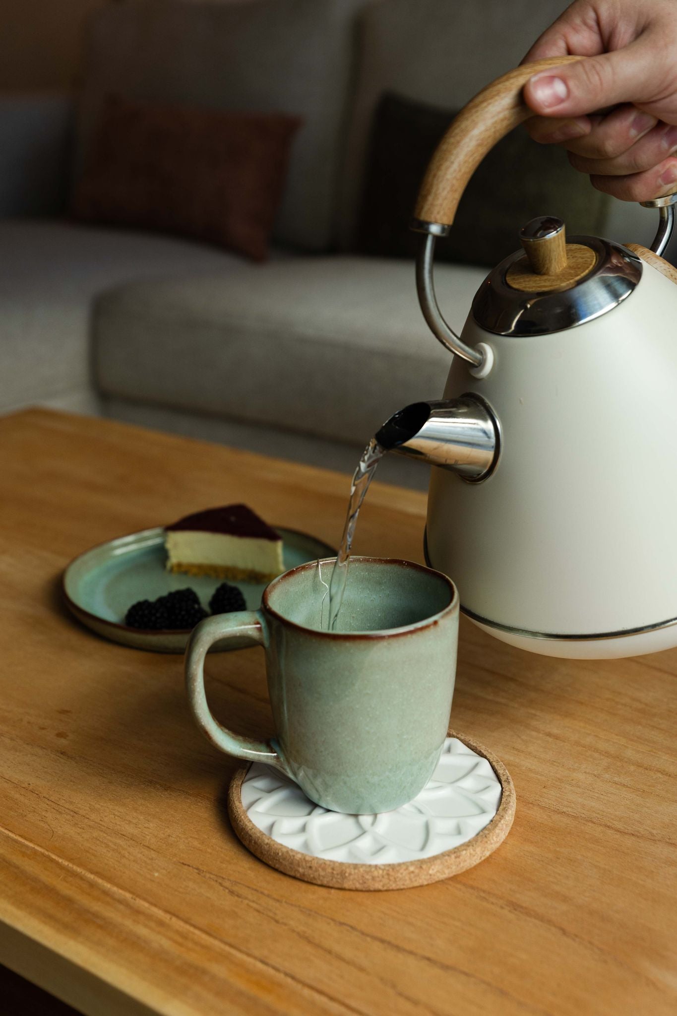 Momento de pausa com a Caneca SERENO verde, recebendo água quente de uma chaleira, destacando o ambiente acolhedor e o design premium da peça.