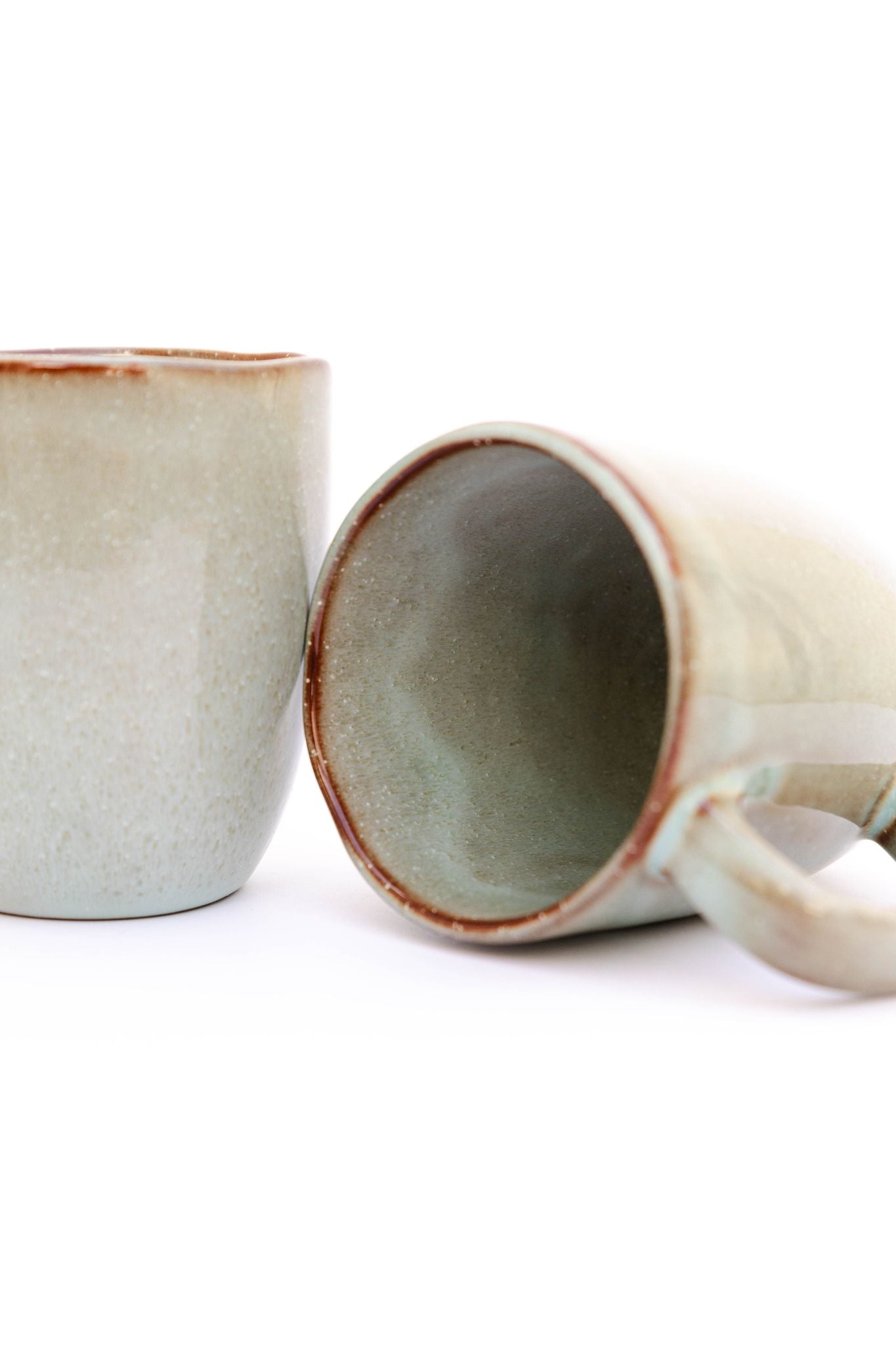 Grande plano da Caneca SERENO evidenciando a textura granulada do vidrado reativo verde e o detalhe do rebordo acobreado, características únicas desta cerâmica artesanal.