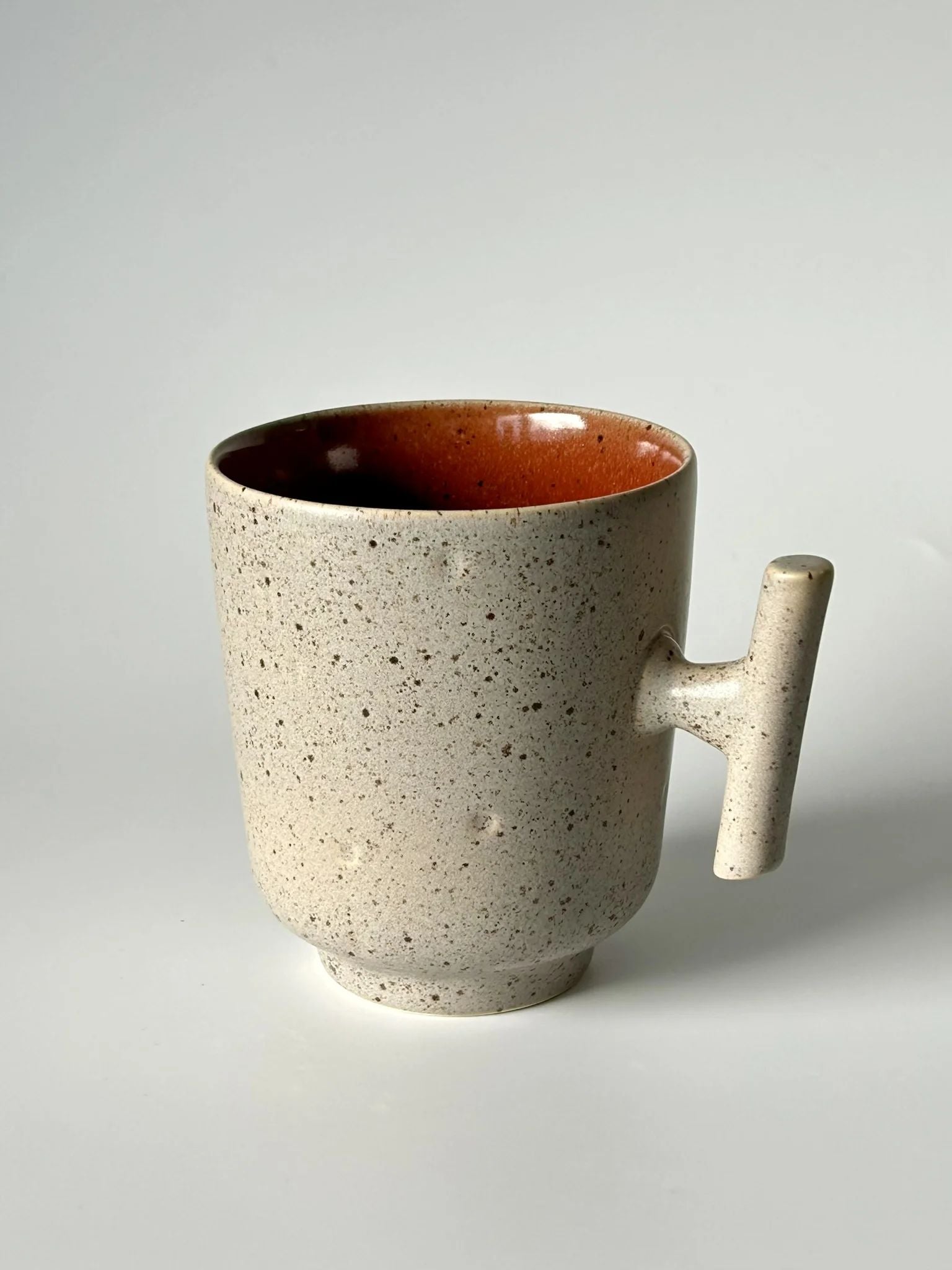 Caneca TERRA em cerâmica portuguesa com exterior granulado areia e interior vermelho quartzo, destacando a asa de design contemporâneo.