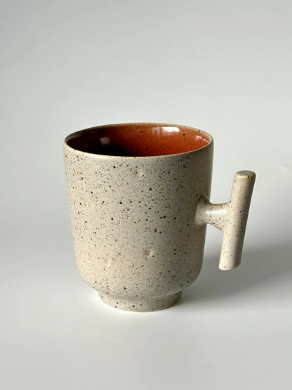 Caneca TERRA em cerâmica portuguesa com exterior granulado areia e interior vermelho quartzo, destacando a asa de design contemporâneo.