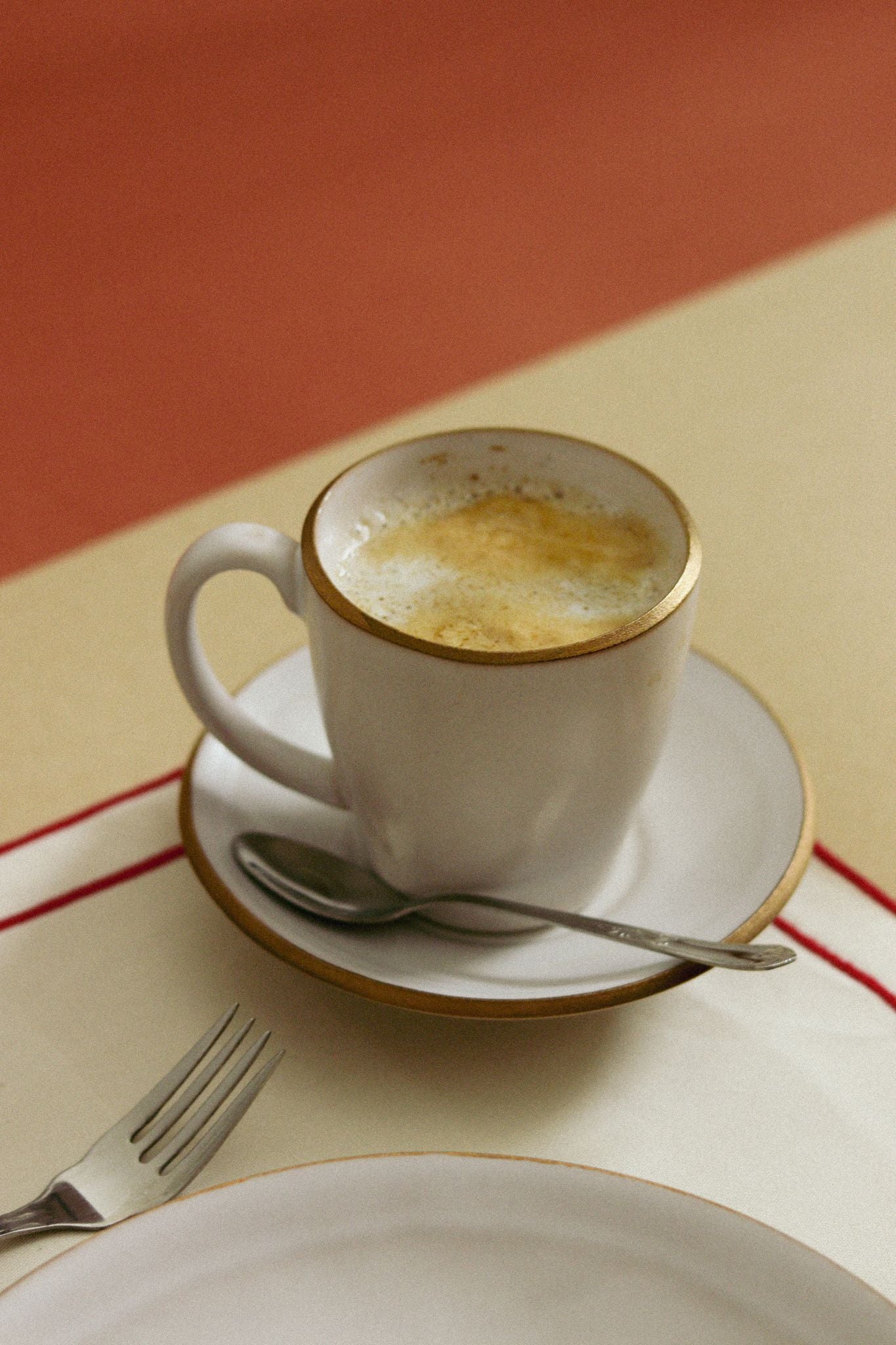 Momento de pausa com a chávena e pires AURA servida com café cremoso numa mesa posta refinada, evocando requinte e bem-estar.