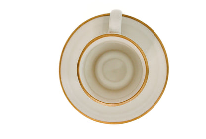Vista zenital (superior) da chávena e pires AURA, mostrando a geometria perfeita do conjunto e o acabamento premium do bordo dourado.