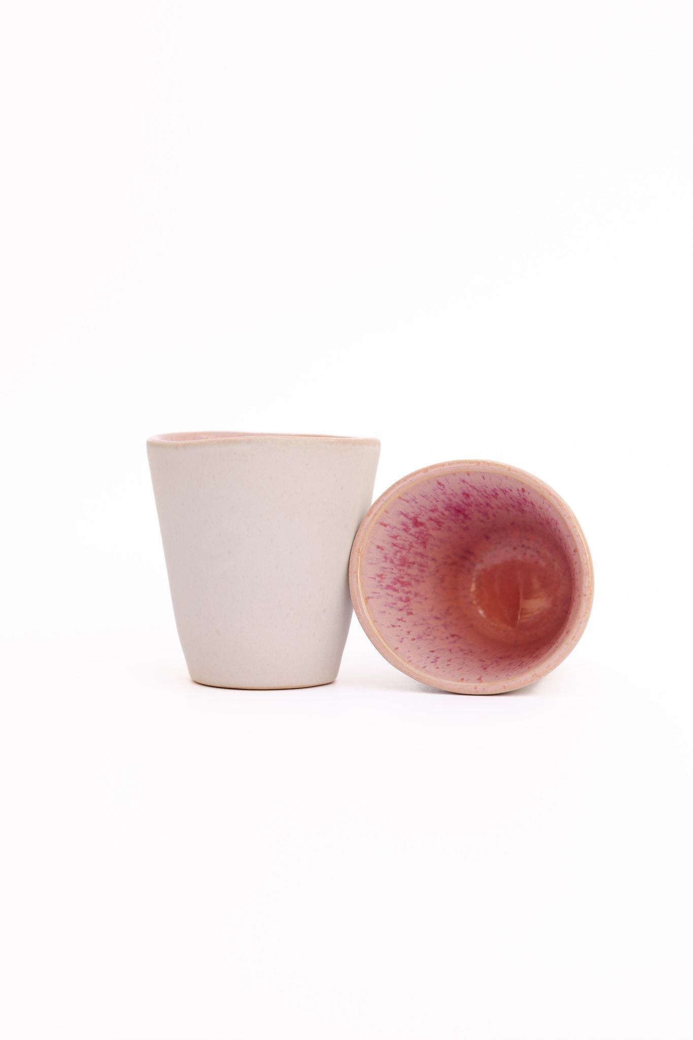 Conjunto de 2 copos de café expresso CORAL em cerâmica rosa e creme, mostrando o interior reativo e o design moderno sem asa.