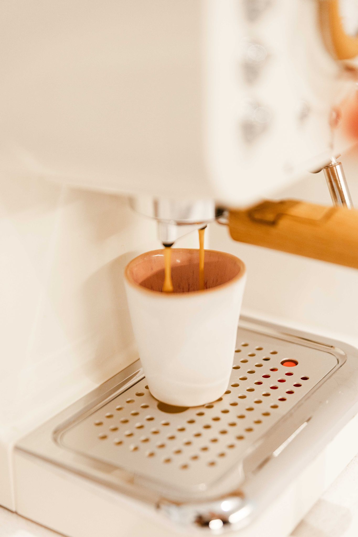 Copo de café CORAL rosa posicionado numa máquina de café expresso de design, capturando o fluxo de café pronto a servir.