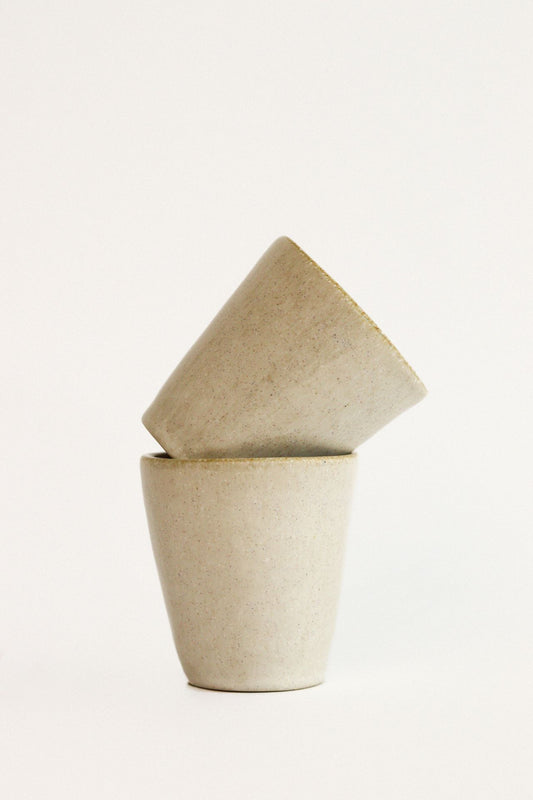 Conjunto de 2 copos de café expresso SERENO creme em cerâmica artesanal, empilhados de forma moderna para destacar o design minimalista e o acabamento liso.