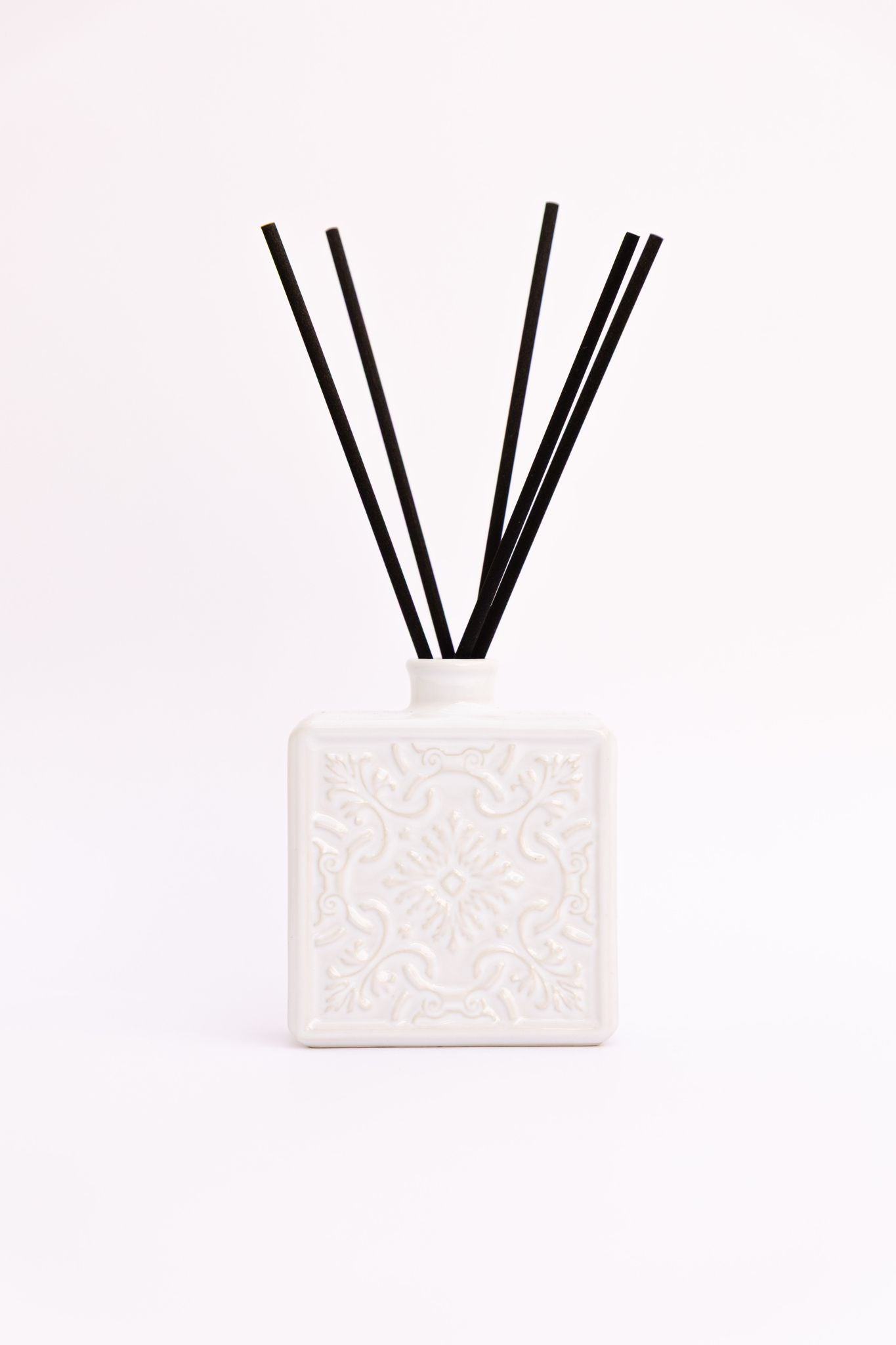Difusor de aromas ALMA em cerâmica branca com varetas de fibra pretas, exibindo o padrão de relevo tradicional sobre fundo branco.