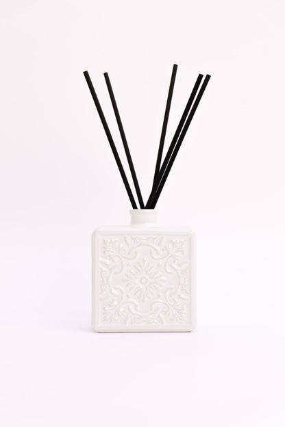 Difusor de aromas ALMA em cerâmica branca com varetas de fibra pretas, exibindo o padrão de relevo tradicional sobre fundo branco.