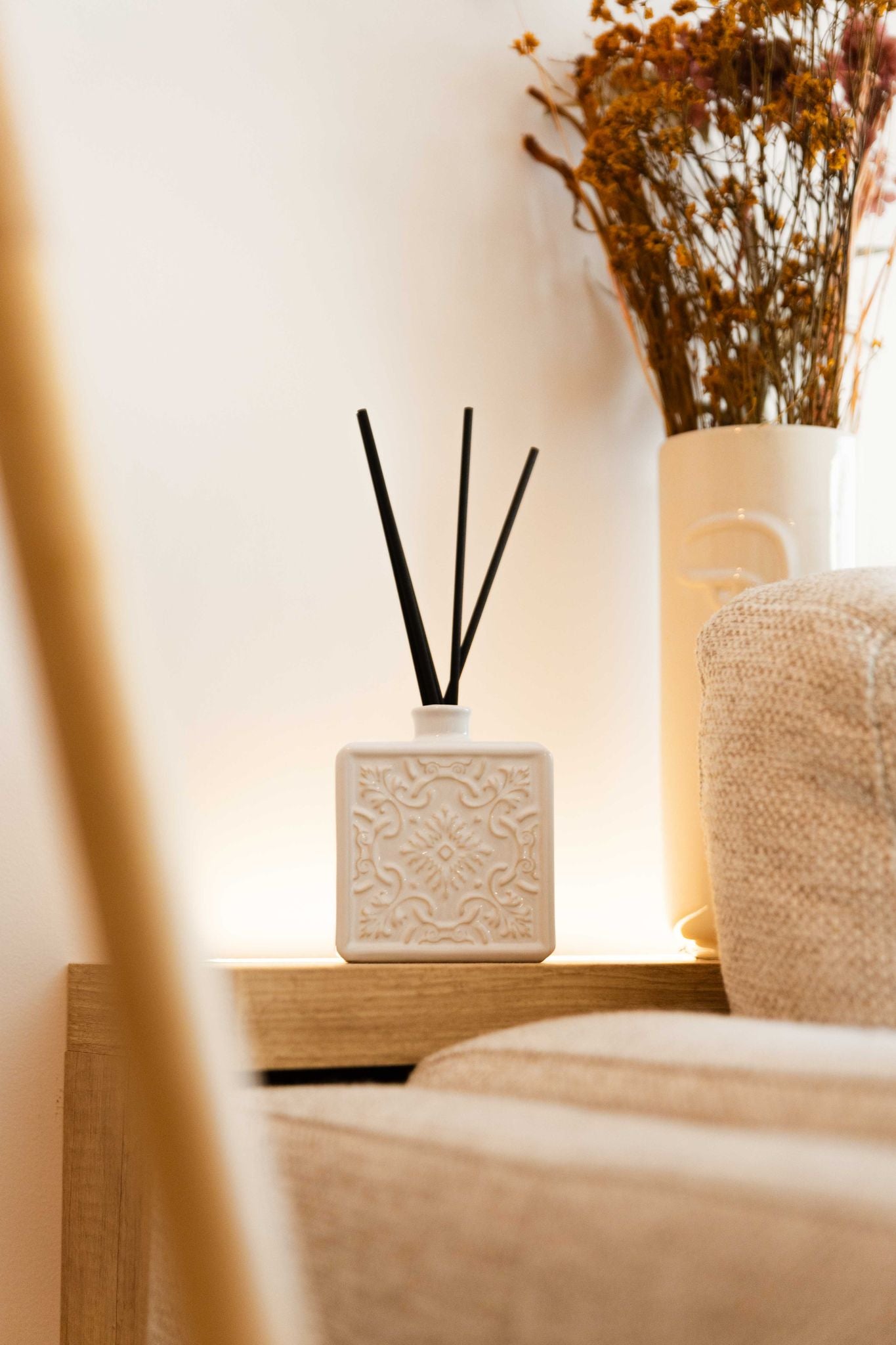 Ambiente acolhedor com o difusor ALMA branco iluminado por luz quente, posicionado numa mesa de cabeceira junto a elementos decorativos.