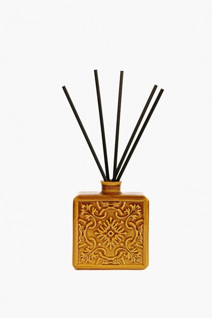 Difusor de fragrâncias ALMA em tom ocre com varetas de fibra, destacando o design clássico e a cor vibrante da cerâmica artesanal.
