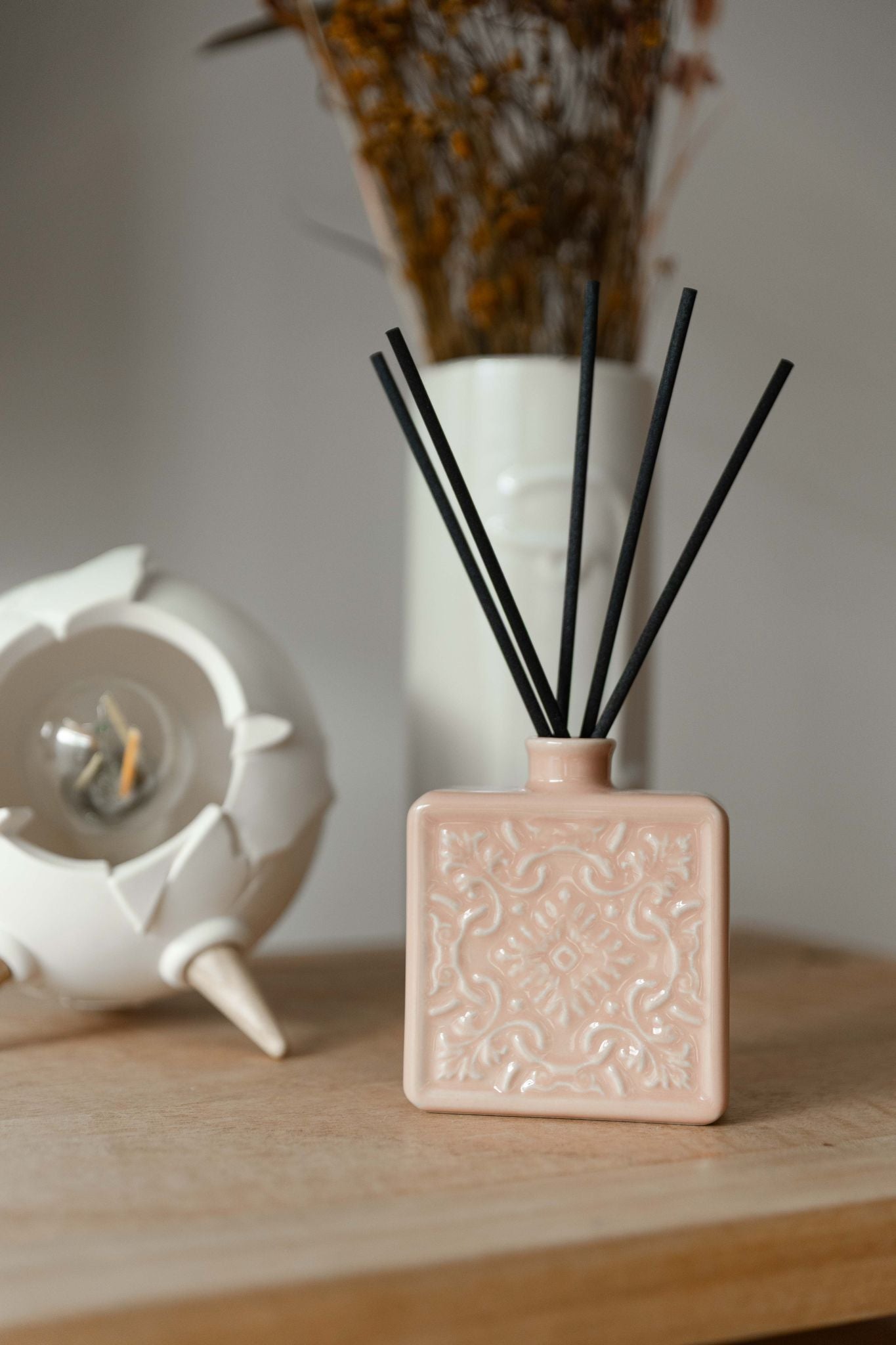 Difusor rosa nude integrado numa decoração minimalista sobre móvel de madeira, transmitindo uma sensação de tranquilidade e aroma a lar.