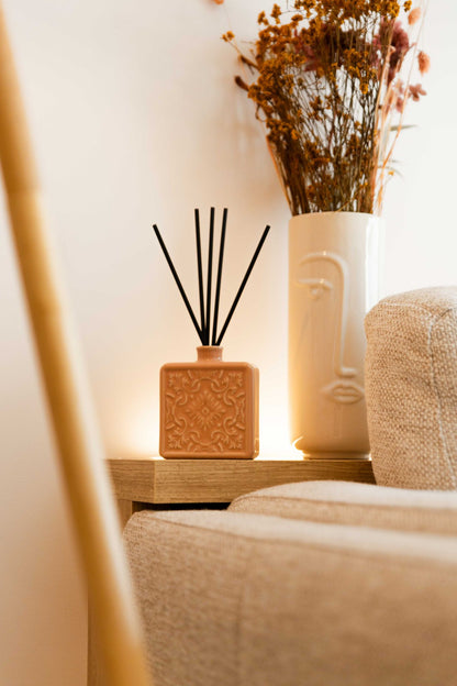Fotografia de lifestyle do difusor ALMA rosa nude junto a um sofá e jarra decorativa, criando um ambiente de bem-estar contínuo.