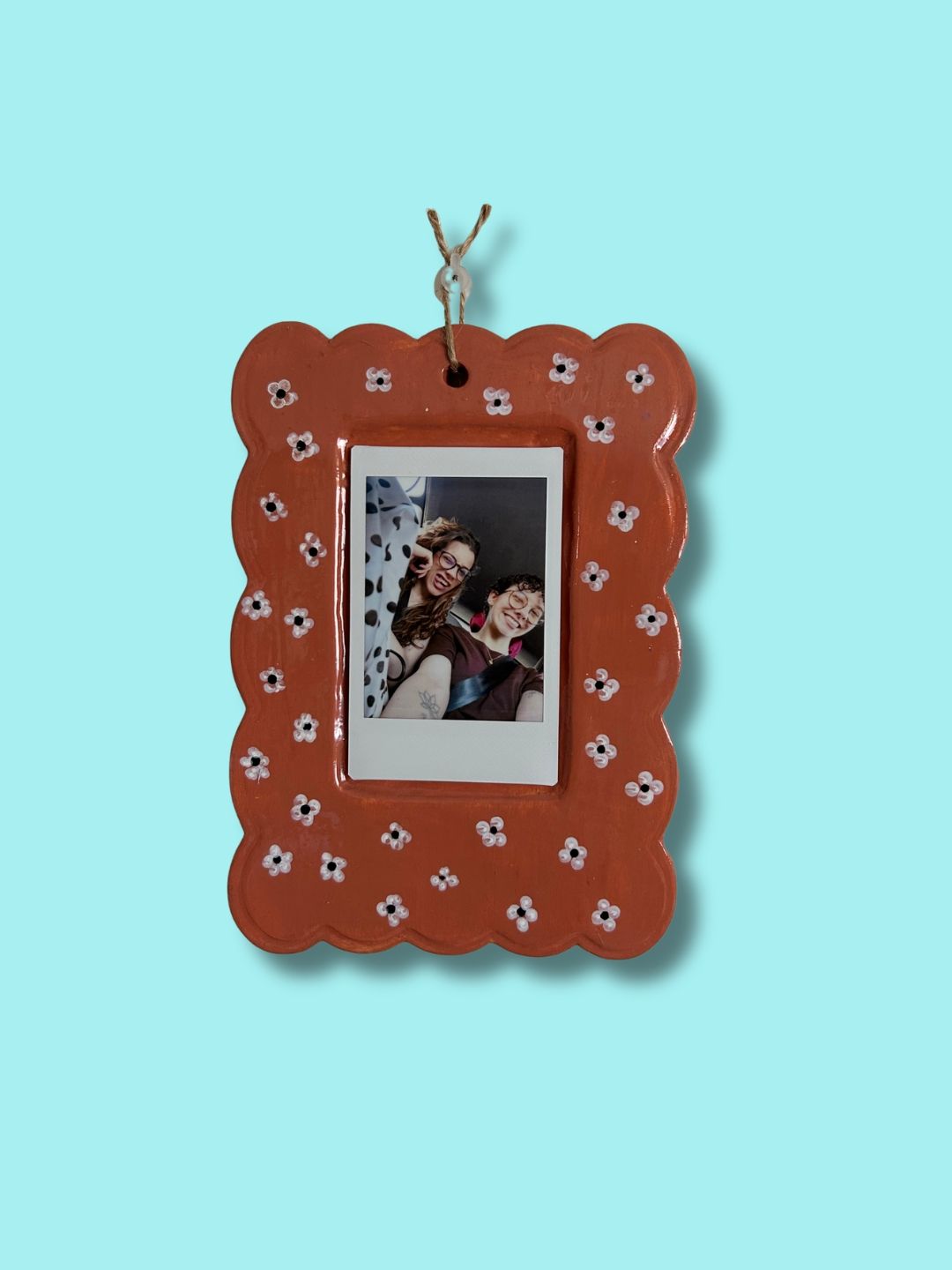 Moldura personalizada em cerâmica fria castanha com pequenas flores pintadas à mão e fotografia de duas pessoas.