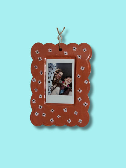 Moldura personalizada em cerâmica fria castanha com pequenas flores pintadas à mão e fotografia de duas pessoas.