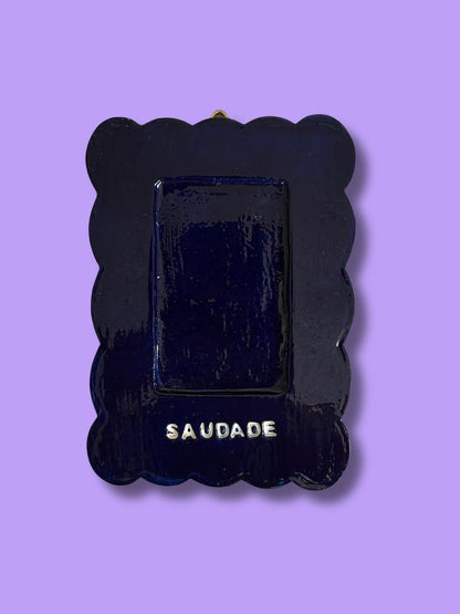 Moldura personalizada em cerâmica fria azul-escura com espaço para fotografia e a palavra “Saudade” pintada à mão.