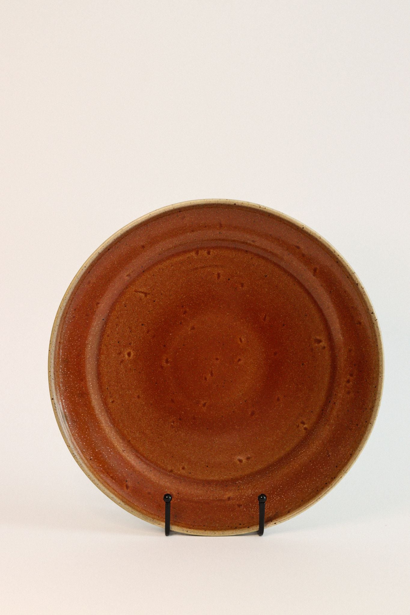 Prato de jantar TERRA 26,5cm em cerâmica vermelha quartzo, apresentado de frente no suporte, exibindo o acabamento rústico e artesanal.