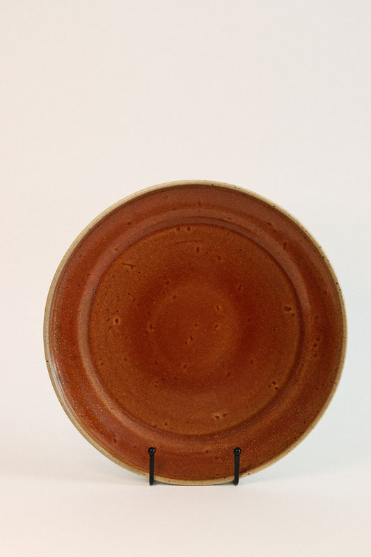 Prato de jantar TERRA 26,5cm em cerâmica vermelha quartzo, apresentado de frente no suporte, exibindo o acabamento rústico e artesanal.