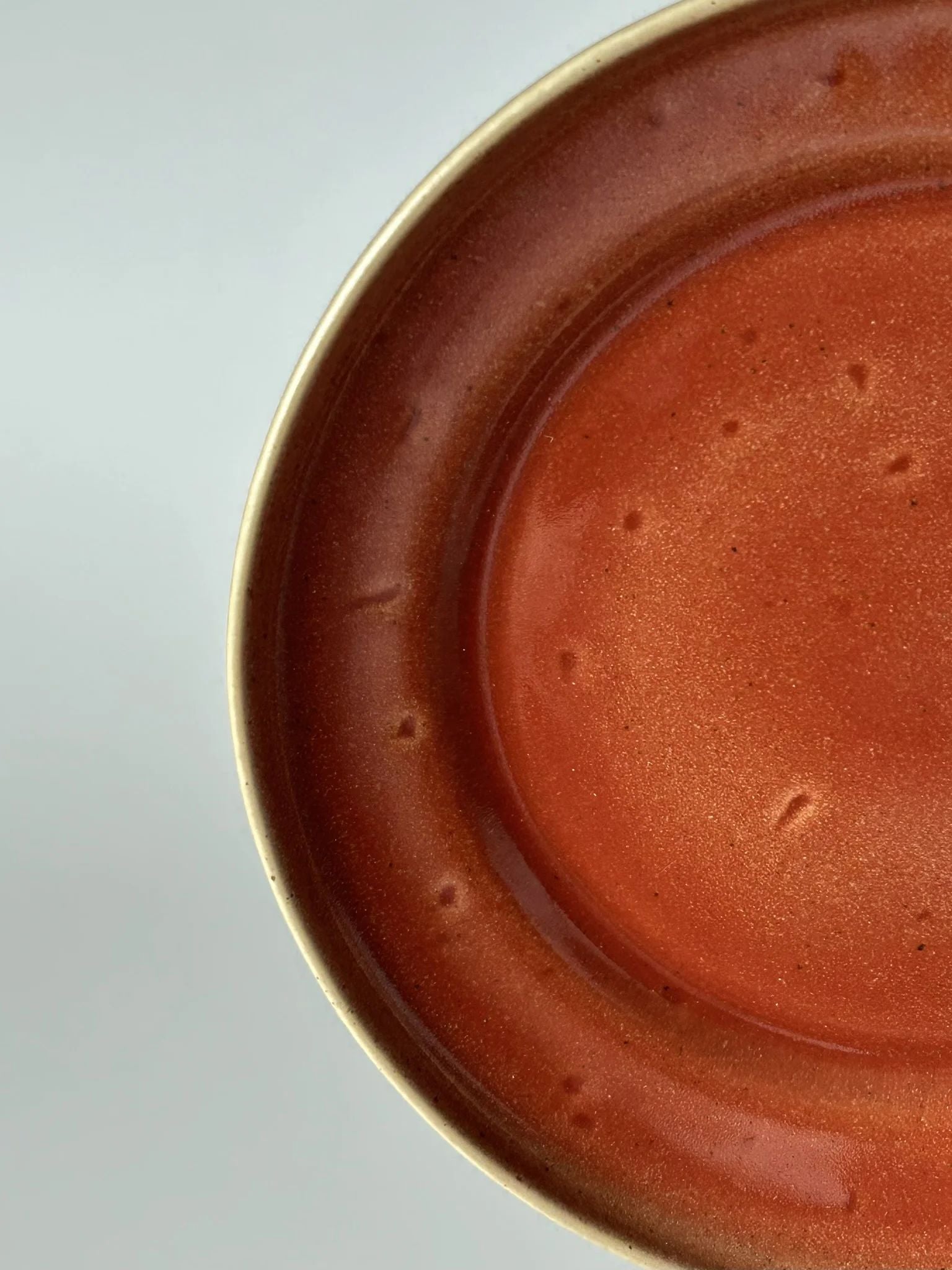Grande plano da superfície do prato de jantar TERRA, destacando as variações naturais do vidrado vermelho e a qualidade do grés fino.