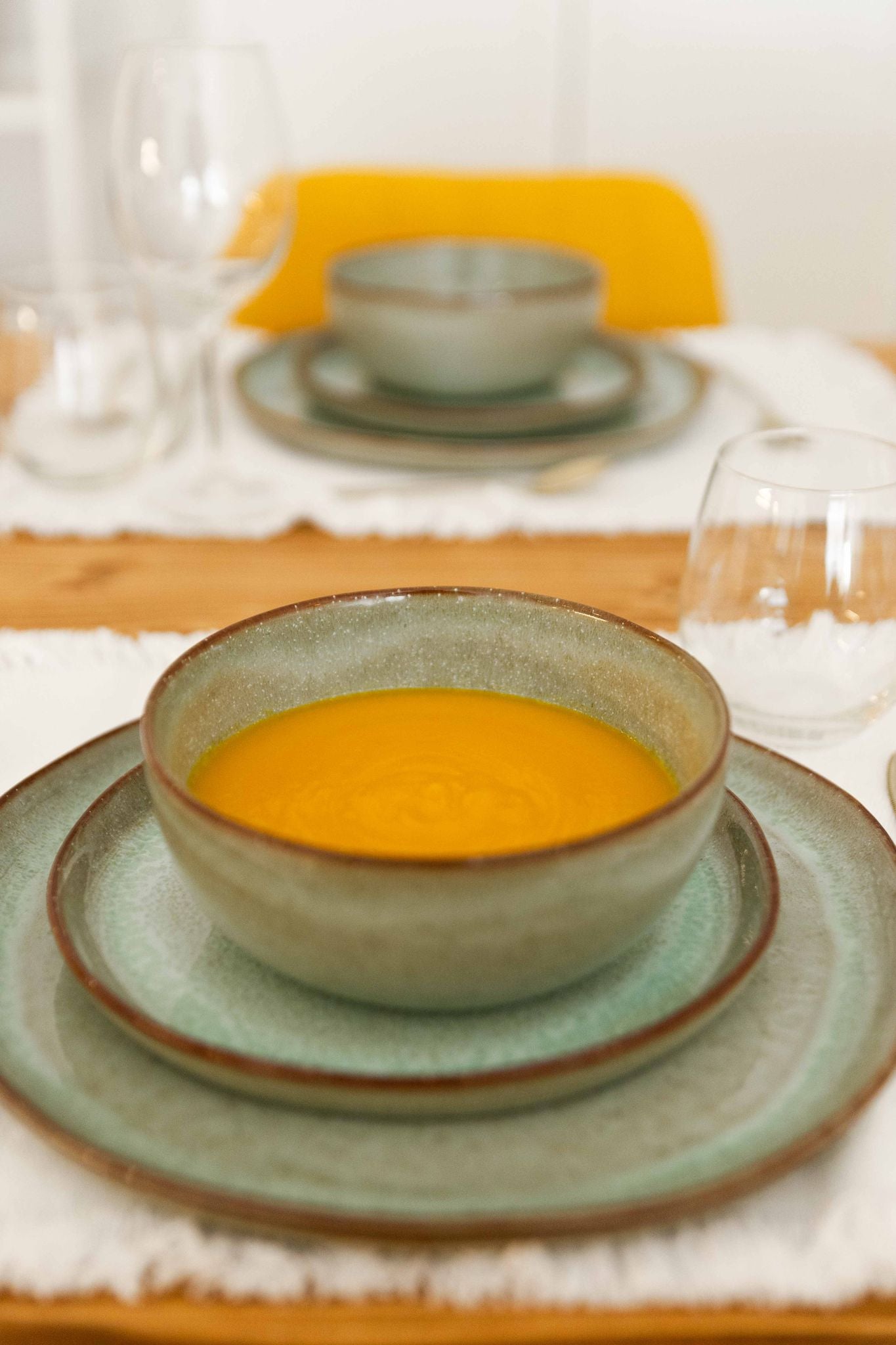 Tigela SERENO verde integrada num serviço de mesa completo, servida com uma sopa quente, ilustrando a funcionalidade e elegância da peça em ambiente de refeição.