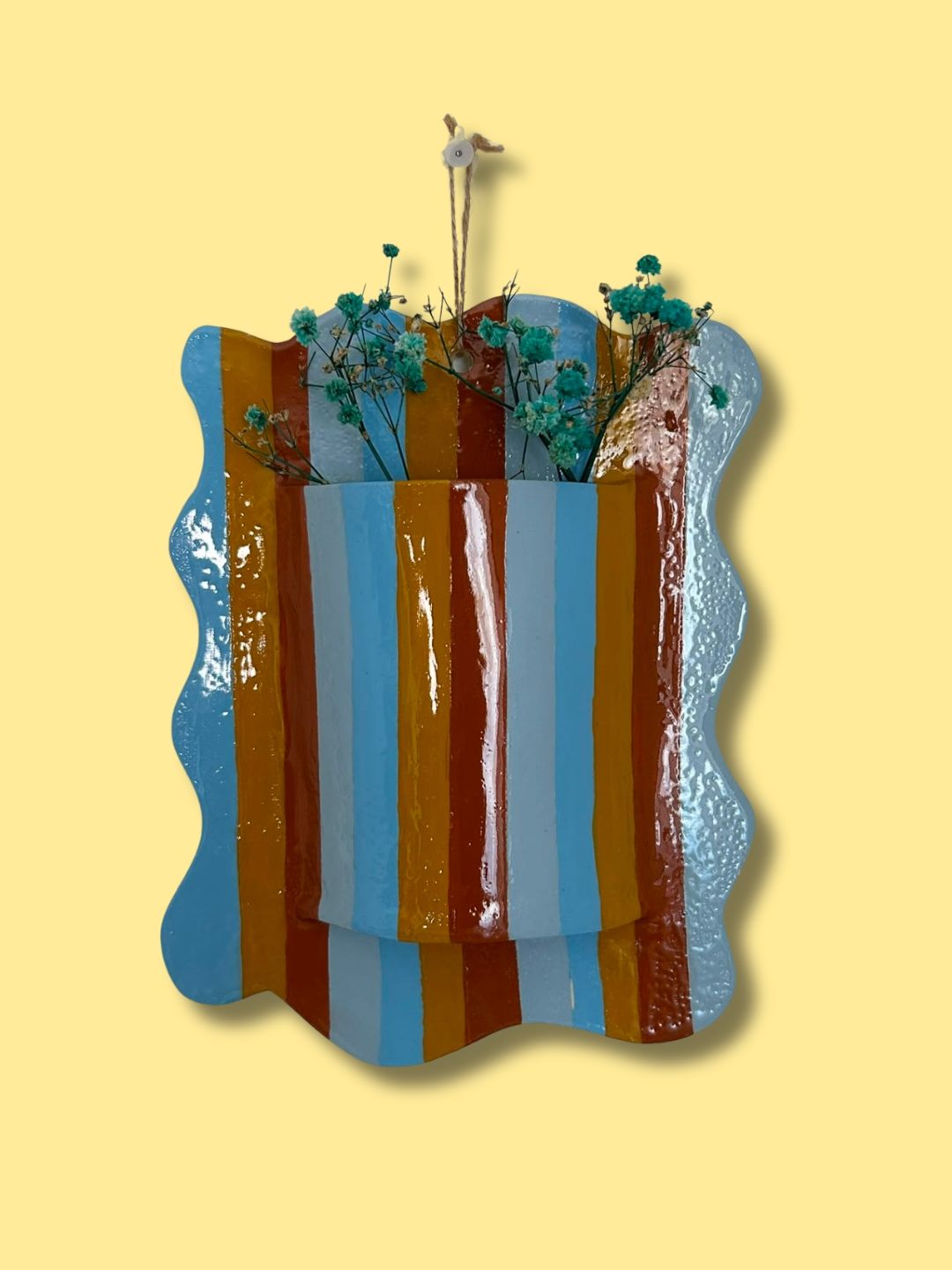 Vaso de parede retangular personalizado em cerâmica fria, com borda ondulada, padrão de riscas coloridas em azul, amarelo e castanho e flores decorativas.